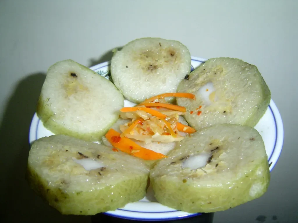 Đĩa bánh tét cắt khoanh lộ phần nhân ở giữa, giữa đĩa là dưa món cà rốt