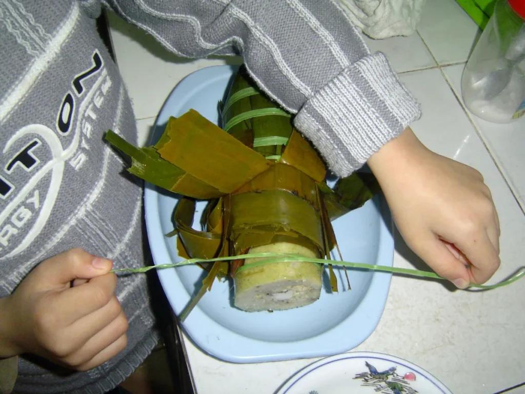 Hai tay kéo sợi dây quấn quanh đòn bánh tét đã bóc một đầu lá để cắt thành khoanh