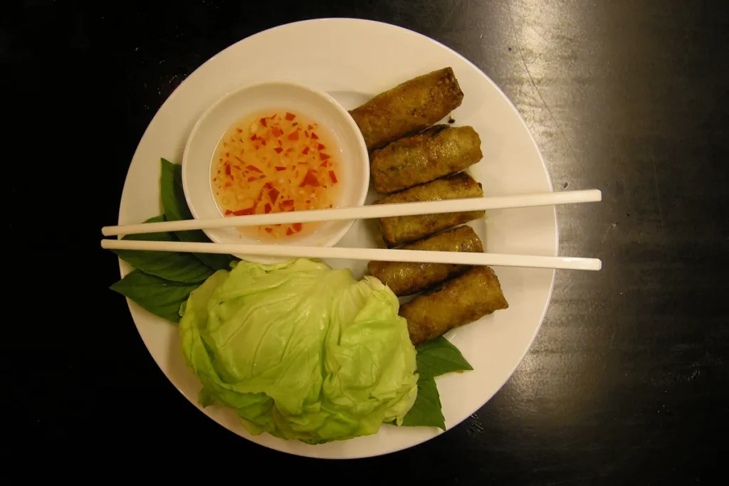 Đĩa chả giò rán vàng kèm xà lách, rau thơm, chén nước mắm chua ngọt và đôi đũa