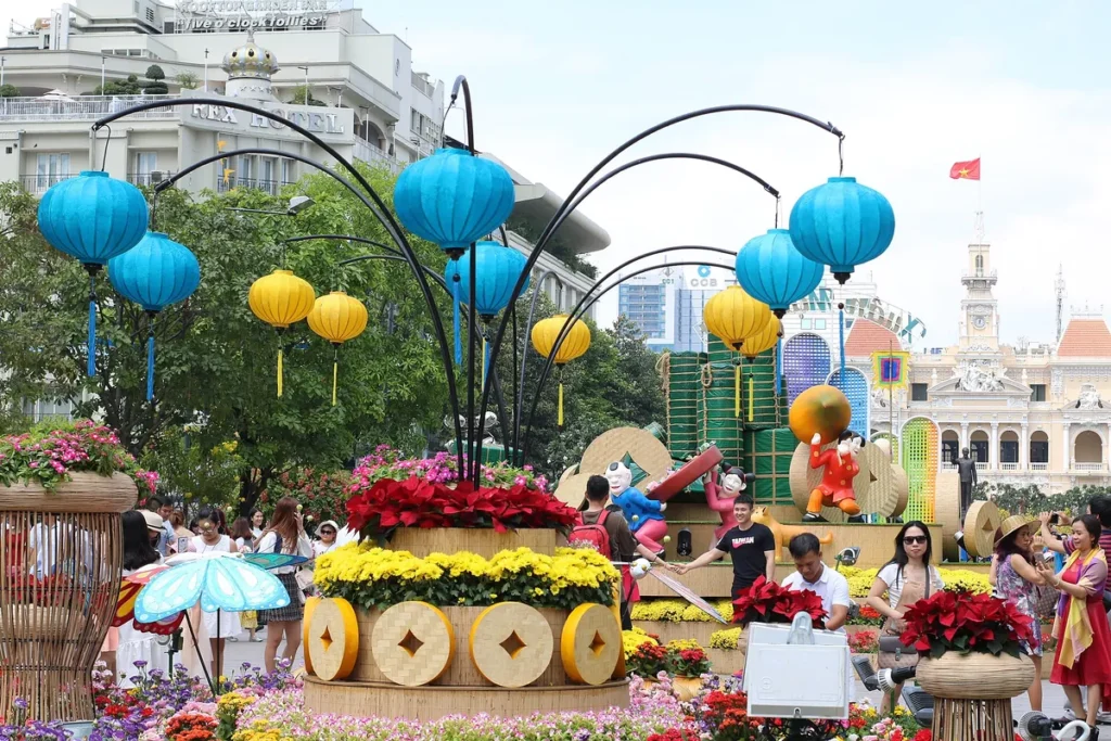 Đèn lồng xanh, vàng treo trên giá uốn cong, phía xa là trụ sở UBND TP.HCM trên đường hoa Nguyễn Huệ
