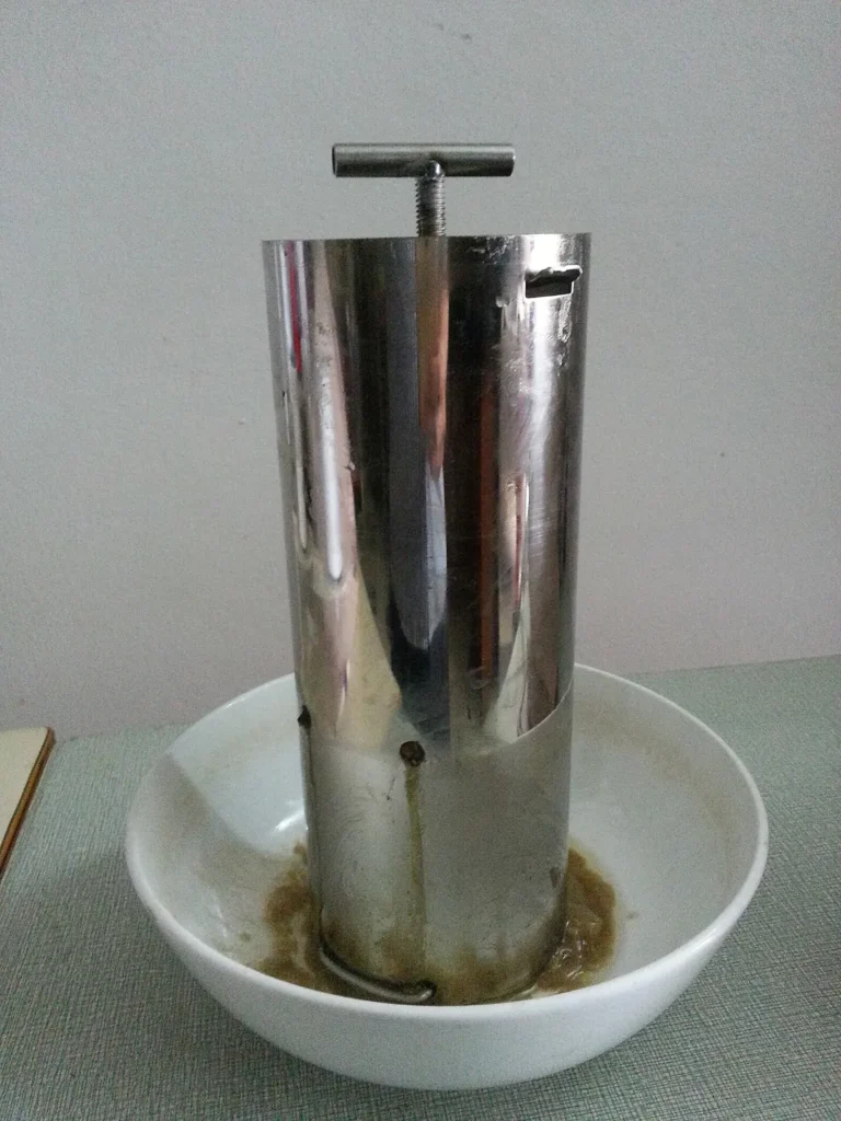 Khuôn inox ép giò thủ có trục vặn phía trên, đặt trong bát sứ hứng nước chảy ra