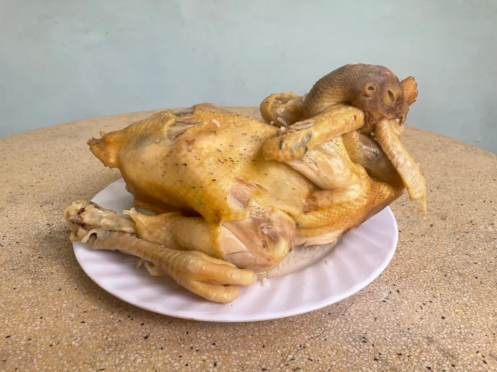 Con gà luộc nguyên con da vàng, đầu quặp về phía cánh, đặt trên đĩa sứ trắng