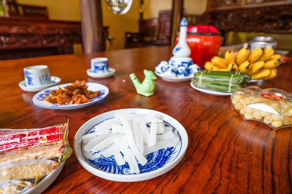 Đĩa mứt bí trắng trong, đĩa mứt gừng, chén trà và bánh chưng bày trên bàn gỗ ngày Tết