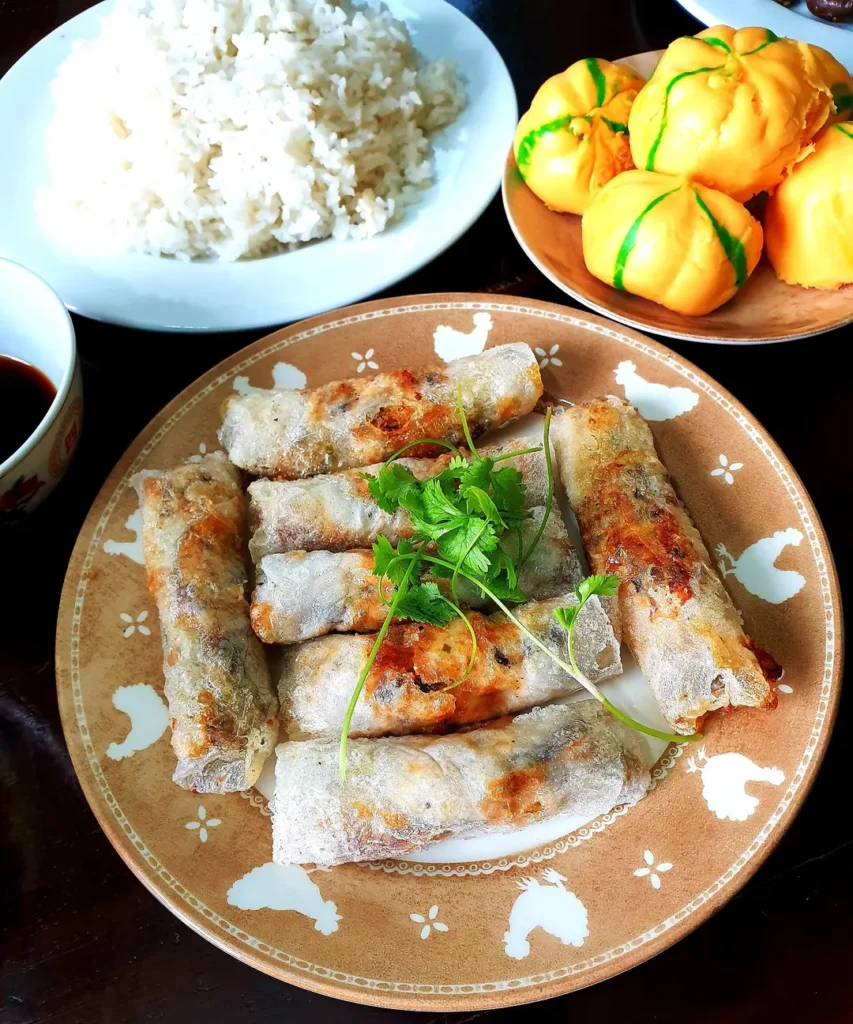 Đĩa nem rán cắt khúc vàng giòn, rắc rau mùi, bên cạnh đĩa cơm và đĩa bánh trong mâm cúng Tết